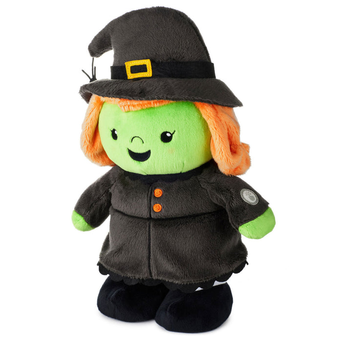 A plush witch doll with a green face, orange hair, and a black hat and dress with small orange buttons, photographed on a plain white background.