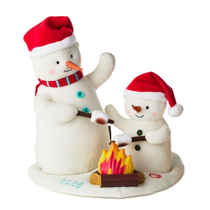 Two snowmen with red hats and scarves sitting around a campfire, on a white background.
