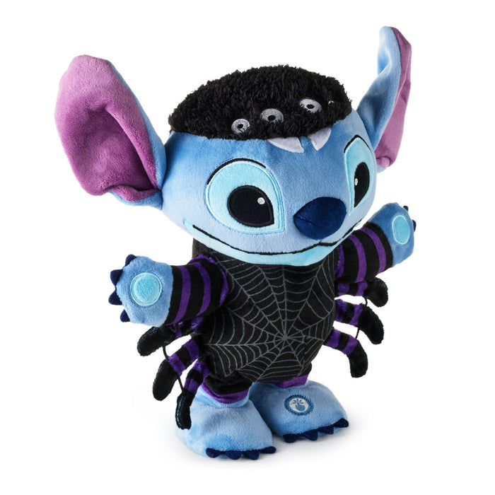 A Stitch plush toy dressed as a spider, featuring a blue body, purple ears and accents, a black spiderweb-patterned body, and a black fuzzy head with three small eyes.