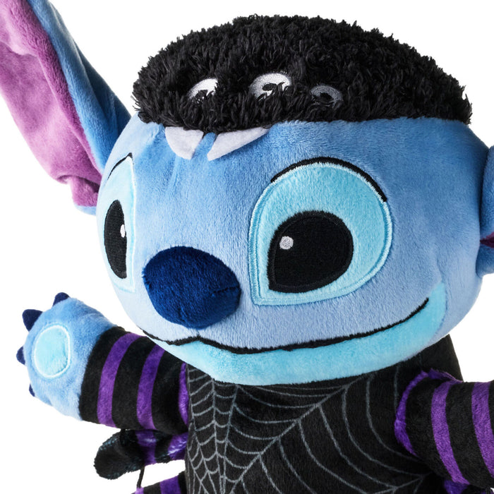 Close-up of a blue plush character costume or doll with large embroidered eyes, black fuzzy hair, purple inner ears, and black-and-purple striped sleeves on a white background.