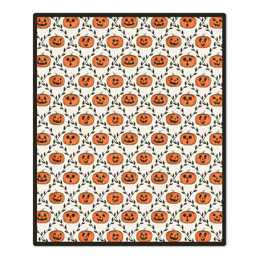 A rectangular area rug with a repeating Halloween pattern of orange jack-o'-lantern pumpkins and black vines on an off-white background, finished with a black border.