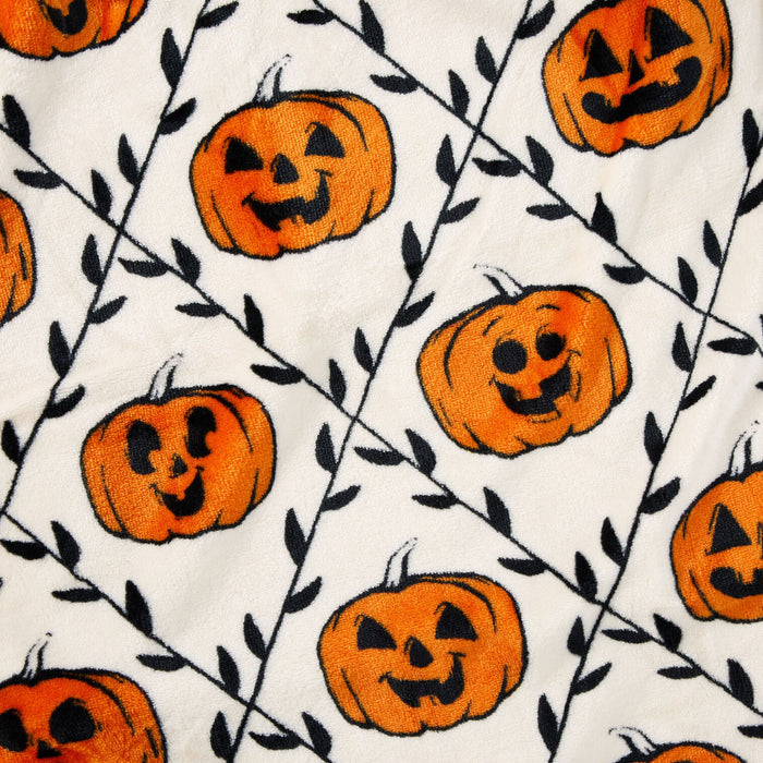 A close-up of a white fabric with an all-over Halloween pattern featuring orange jack-o'-lantern pumpkins and black vine branches.