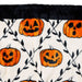 A close-up of a plush blanket featuring a Halloween pattern with orange jack-o'-lantern pumpkins and black leafy vines on an off-white background, finished with a black faux-fur trim.
