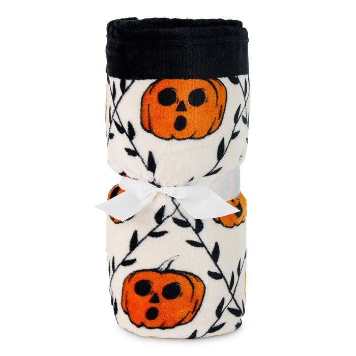 A rolled-up fleece blanket featuring a black top border and an orange pumpkin print on an off-white background, tied with a white ribbon.