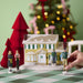Decorative Christmas scene with a house, trees, and people on a checkered surface.