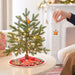 Small decorated Christmas tree with a person hanging an ornament in a cozy living room.