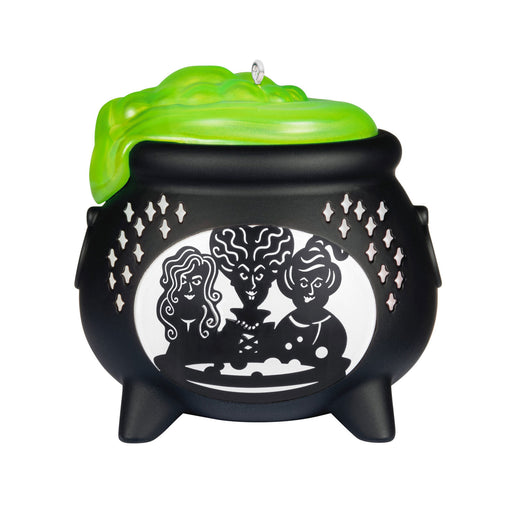 Black cauldron-shaped candle with green lid featuring silhouettes of three figures on a white background