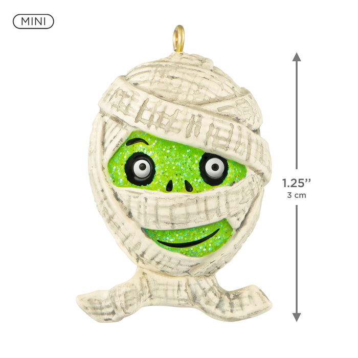 Miniature mummy-shaped ornament with green face and white bandages, featuring dimensions on a white background.