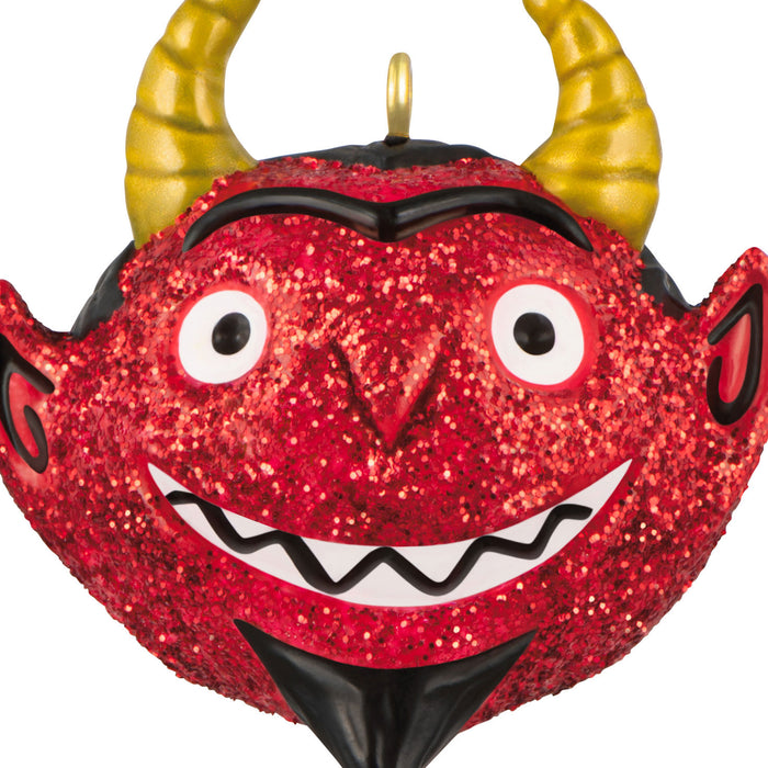 Red glittery monster ornament with yellow horns on a white background