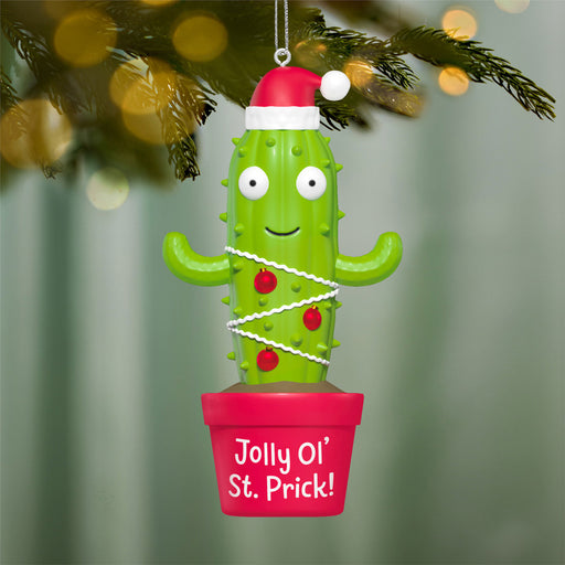 Cactus ornament with a Santa hat and 'Jolly Ol' St. Prick!' text, hanging on a Christmas tree.