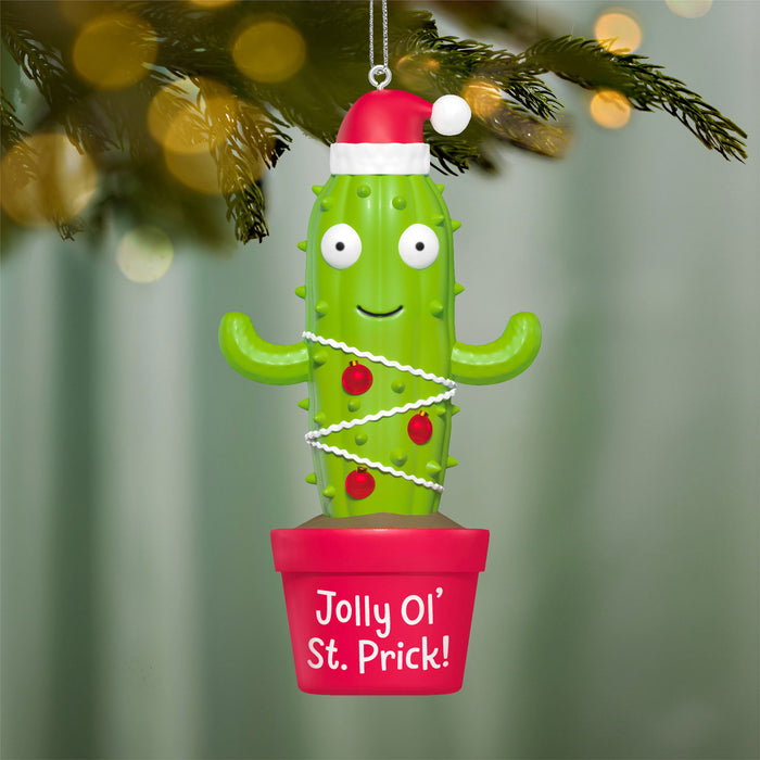 Cactus ornament with a Santa hat and 'Jolly Ol' St. Prick!' text, hanging on a Christmas tree.