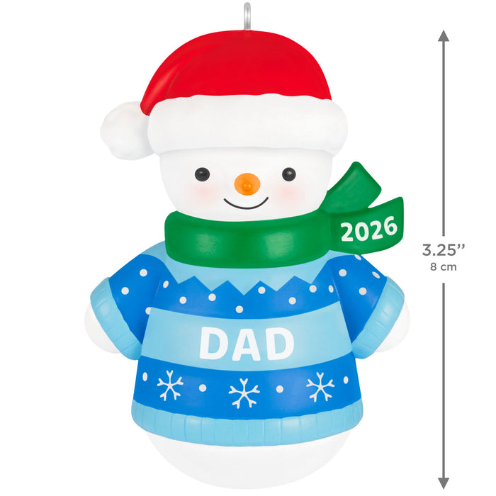 Snowman ornament with a blue sweater labeled 'DAD' and a red hat, wearing a green scarf with '2026'.