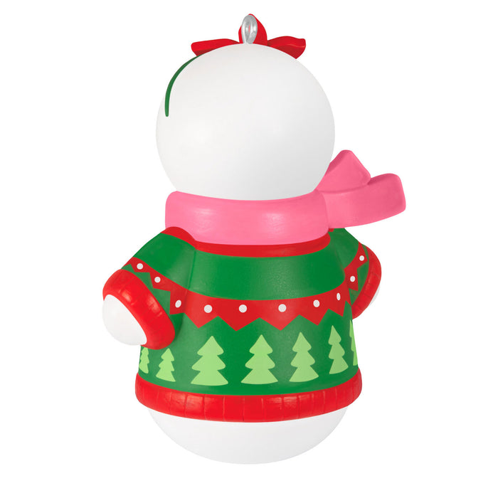 Decorative Christmas snowman ornament with a pink scarf and green sweater with tree pattern on a white background.