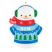 Christmas ornament of a snowman wearing a blue sweater with green trees, red scarf, and green earmuffs on a white background.