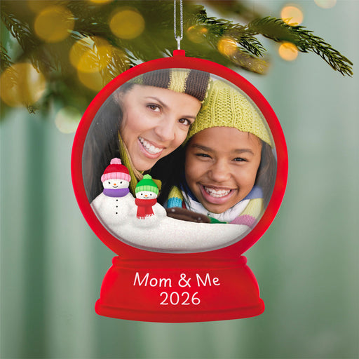 Christmas ornament with a photo of a woman and a child, snowmen, and 'Mom & Me 2026' text, hanging on a decorated tree.