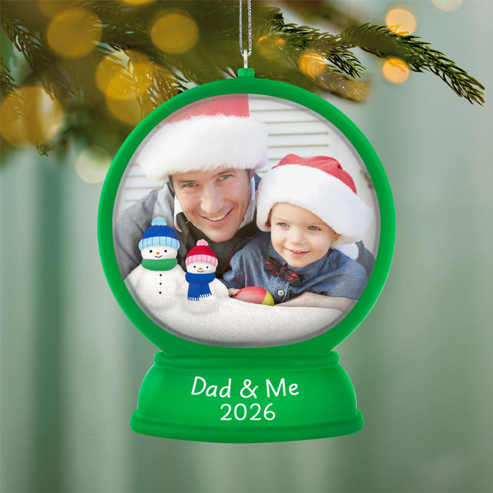 Personalized Christmas ornament with a photo of a man and a child wearing Santa hats, surrounded by snowmen, against a blurred Christmas tree background.