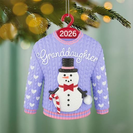 Christmas ornament of a sweater with 'Granddaughter' and a snowman, hanging on a tree.