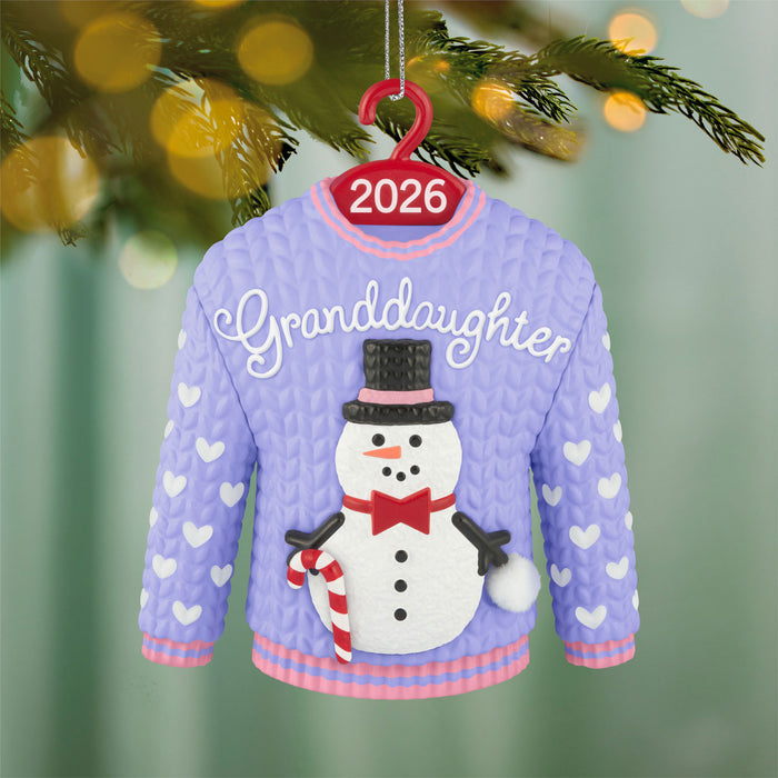 Christmas ornament of a sweater with 'Granddaughter' and a snowman, hanging on a tree.