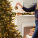 Person decorating a Christmas tree with an ornament in a festive living room.