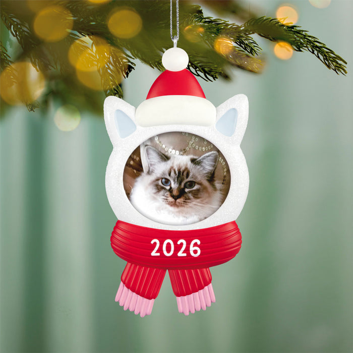 Christmas ornament with a cat's face, Santa hat, and red scarf, hanging on a tree.