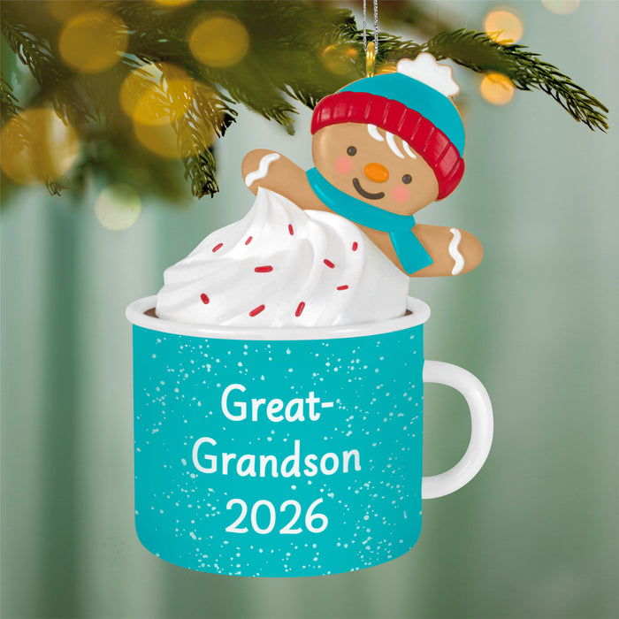 Christmas ornament with gingerbread man on a mug labeled 'Great-Grandson 2026' against a blurred Christmas tree background.