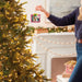 Person hanging a decorative ornament on a Christmas tree in a festive living room.
