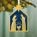 Decorative Christmas ornament with gold nativity scene on a blue background, hanging from a tree.