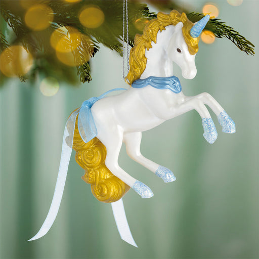 Decorative unicorn ornament with gold hair and blue accents hanging on a tree.
