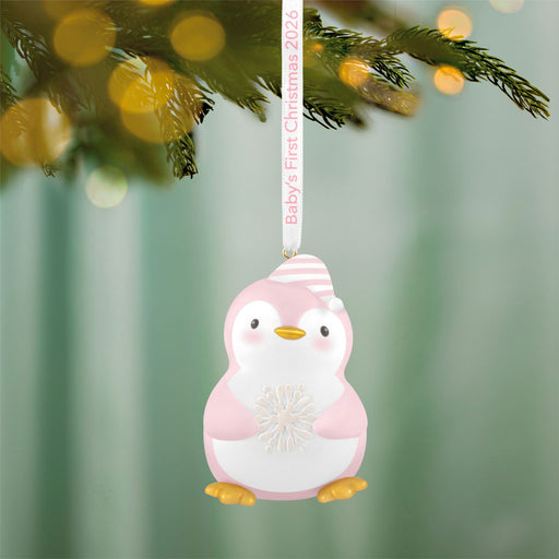 Pink penguin ornament with 'Baby's First Christmas 2026' text on a blurred green background
