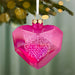 Pink heart-shaped ornament with 'Our First Christmas Together' text on a blurred Christmas tree background.