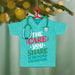 Decorative ornament shaped like a turquoise shirt with a stethoscope, featuring text on a blurred green background.