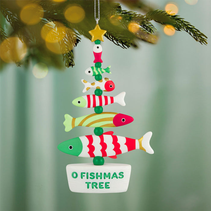 Colorful fish-shaped Christmas tree ornament hanging on a branch with blurred lights in the background.