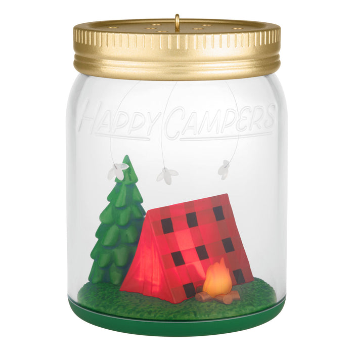 Decorative candle in a jar with a gold lid, featuring a red tent, green tree, and campfire inside.