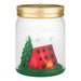 Decorative candle in a jar with a gold lid, featuring a red tent, green tree, and campfire inside.