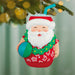 Santa Claus ornament in a beach-themed outfit with a ball, hanging on a Christmas tree.