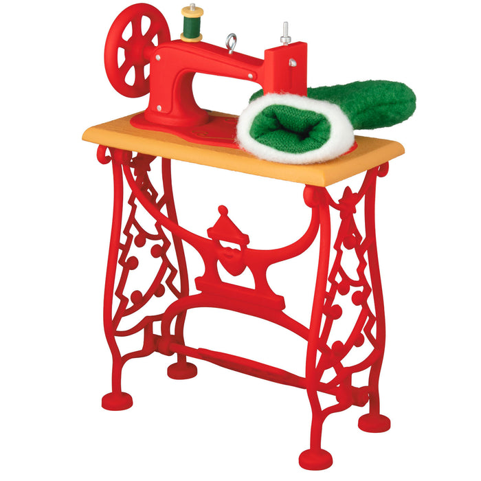 Red miniature sewing machine with a wooden table on a white background