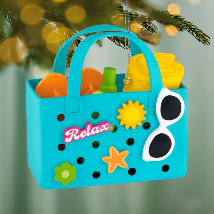 Colorful beach-themed ornament with sand toys and 'Relax' text, hanging against a blurred green background.