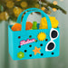 Colorful beach-themed ornament with sand toys and 'Relax' text, hanging against a blurred green background.