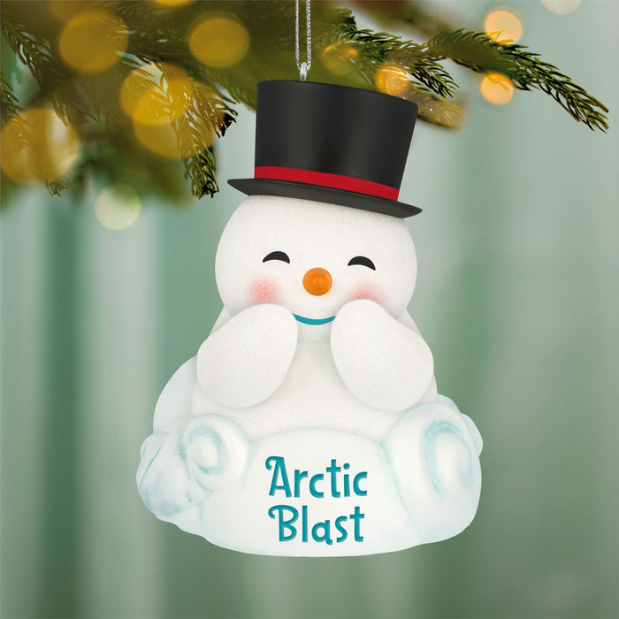Snowman ornament with a top hat and 'Arctic Blast' text, hanging on a Christmas tree.