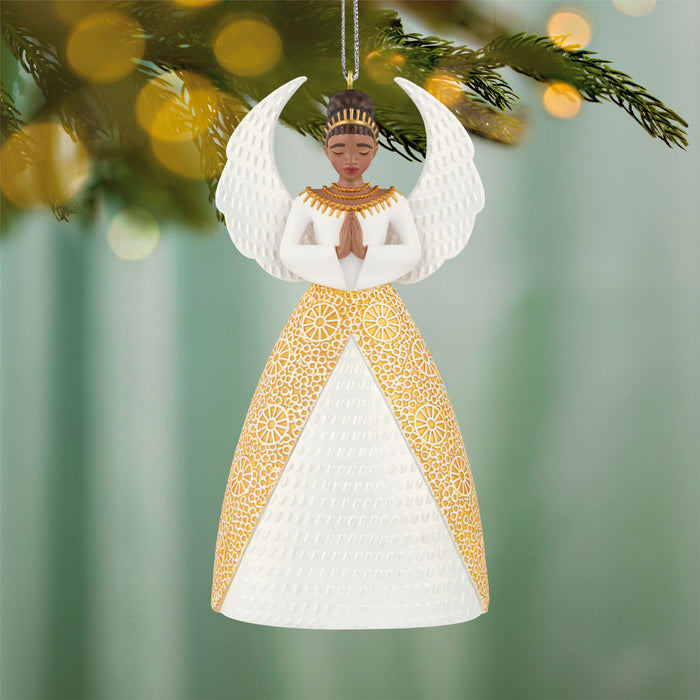 Decorative angel ornament with gold and white dress hanging on a tree branch.