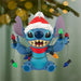 Blue cartoon character wearing a Santa hat with Christmas lights on a tree branch.