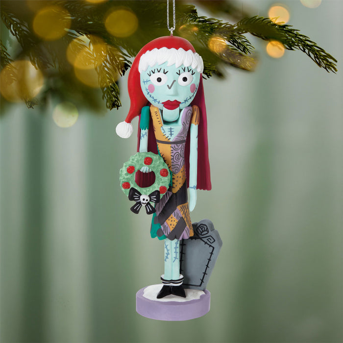Decorative Christmas ornament of a character with a red hat and wreath, standing on a purple base, against a blurred green background.