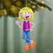 Cartoon character ornament with yellow hair, purple shirt, blue pants, and orange sandals hanging from a Christmas tree.