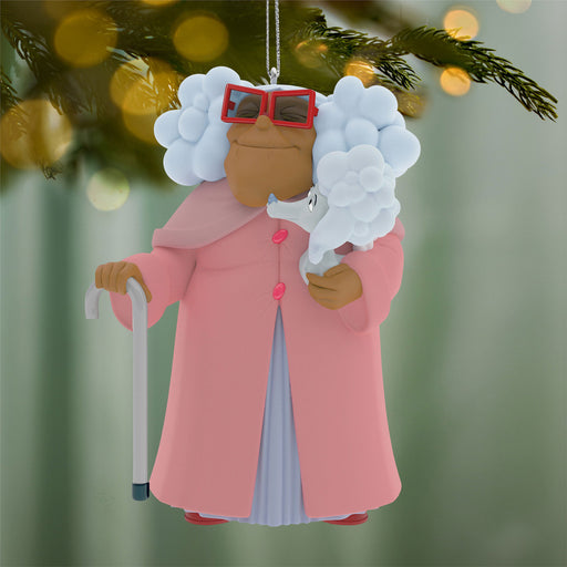 Decorative ornament of a person with white hair, red glasses, and a pink coat holding a cane, hanging on a Christmas tree.