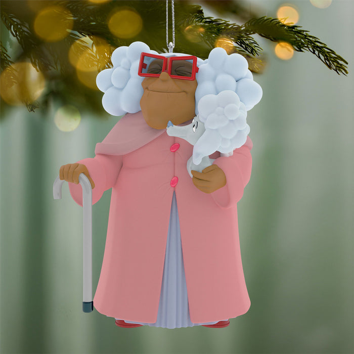Decorative ornament of a person with white hair, red glasses, and a pink coat holding a cane, hanging on a Christmas tree.