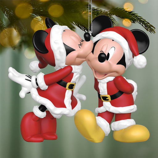 Decorative ornament of Mickey and Minnie Mouse in Santa outfits against a blurred Christmas tree background.