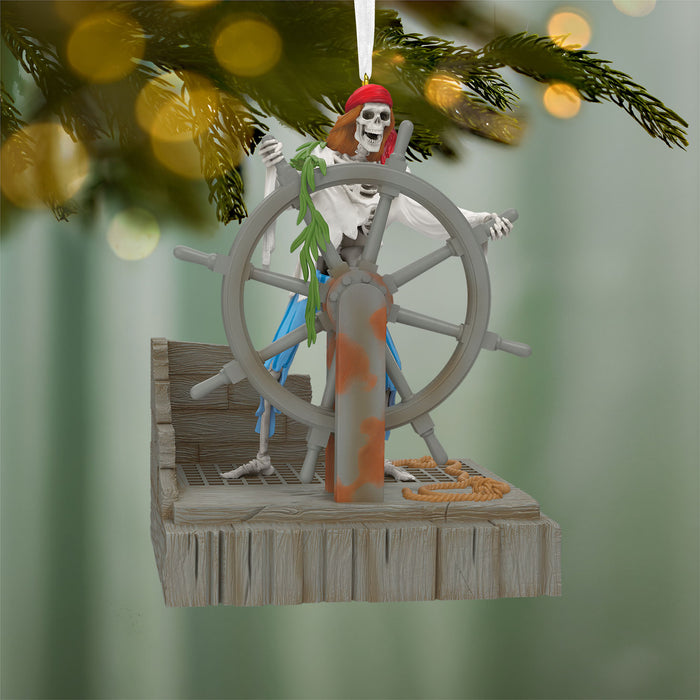 Decorative Christmas ornament with a skeleton at the helm of a ship, hanging from a tree.