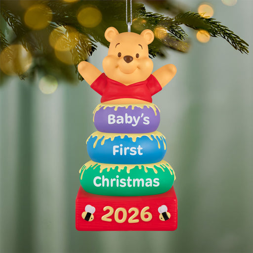 Decorative ornament with Winnie the Pooh for 'Baby's First Christmas 2026' on a tree.