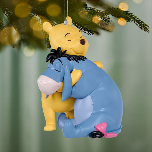 Decorative ornament of a Winnie the Pooh and Eeyore hugging, hanging on a Christmas tree.