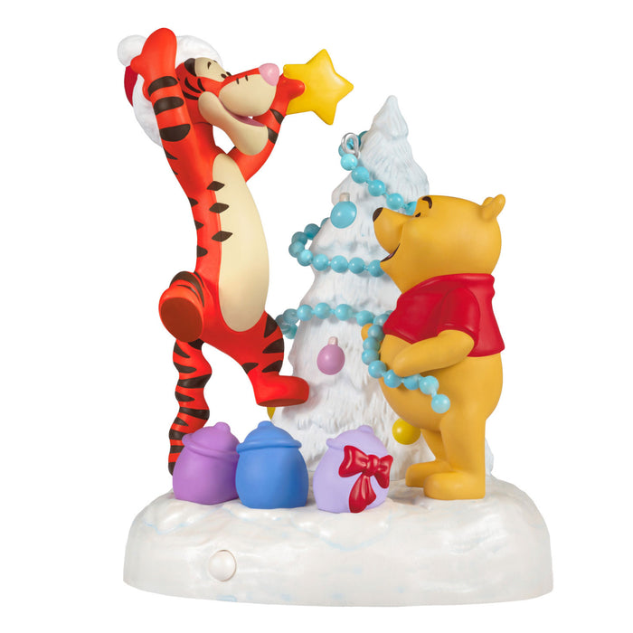 Figurine of Winnie the Pooh and Tigger decorating a Christmas tree with colorful ornaments on a white background.